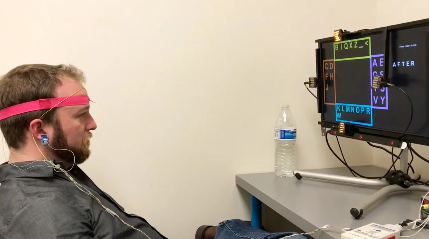 Man wearing a neural sensing headset while viewing a computer display