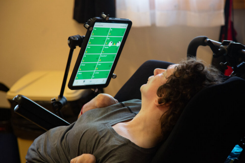 Woman reclining in a power wheelchair while using a mounted tablet communication device
